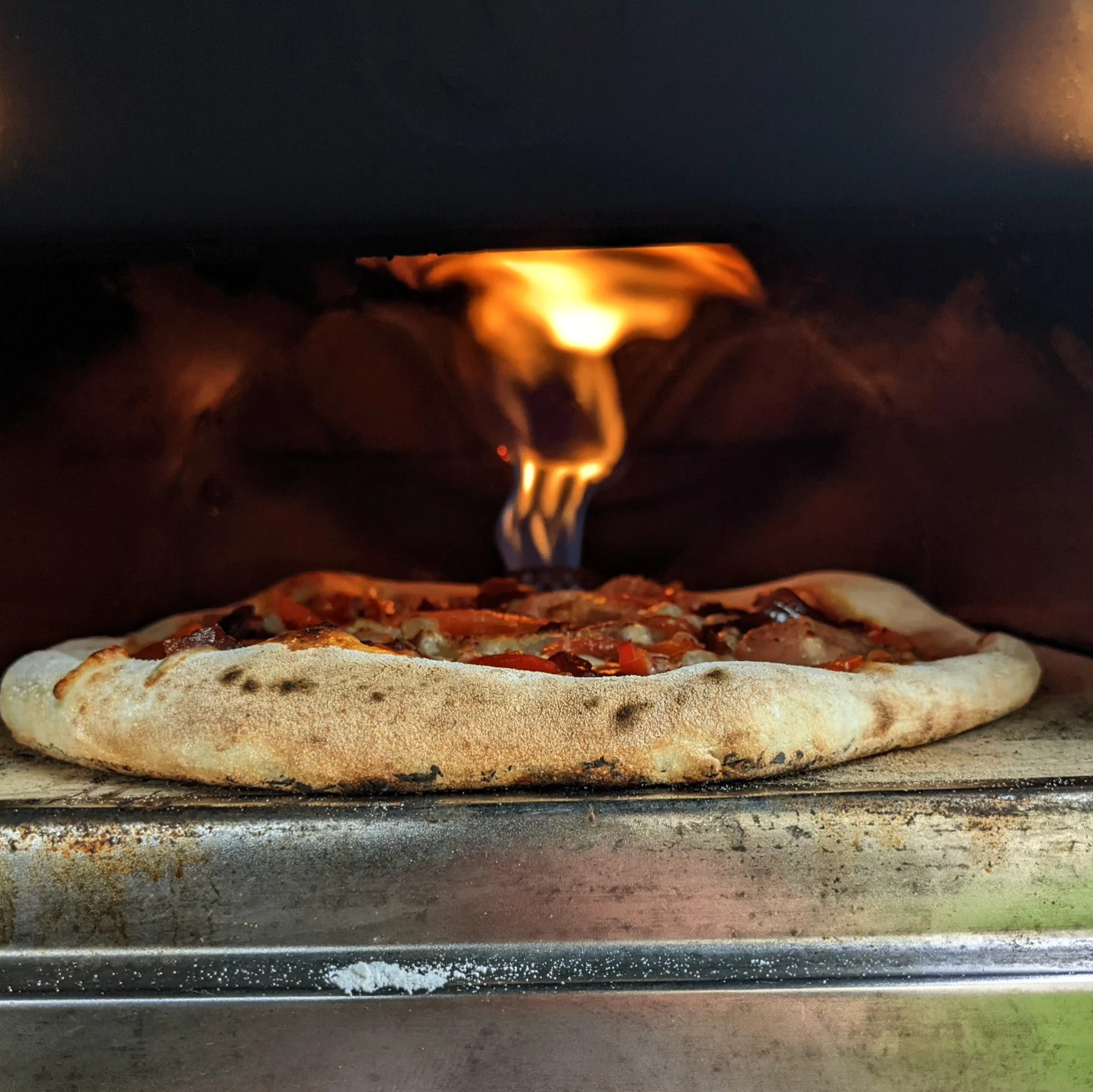 Wood-fired pizza emerging from the oven with flames